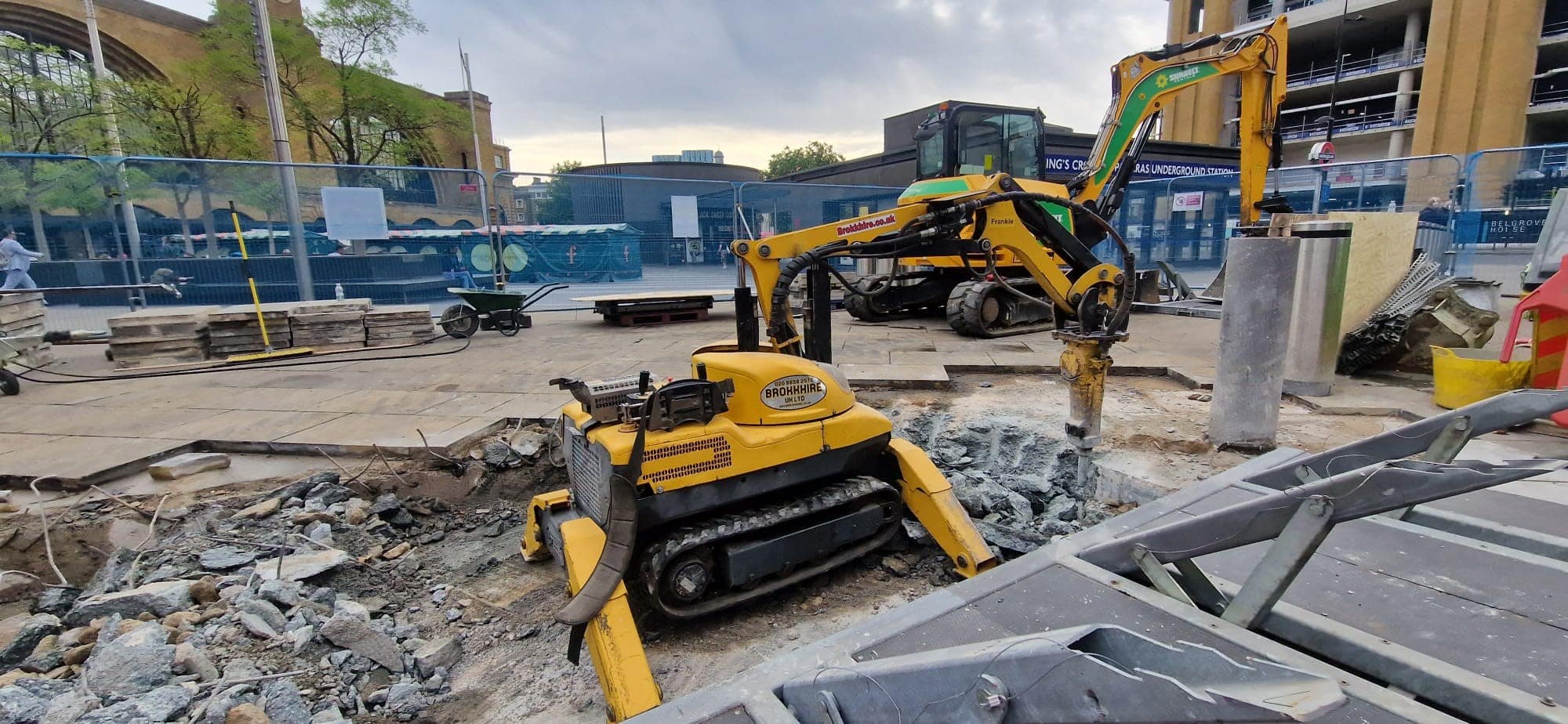 Yellow construction equipment working on a building site with rubble and machinery around.