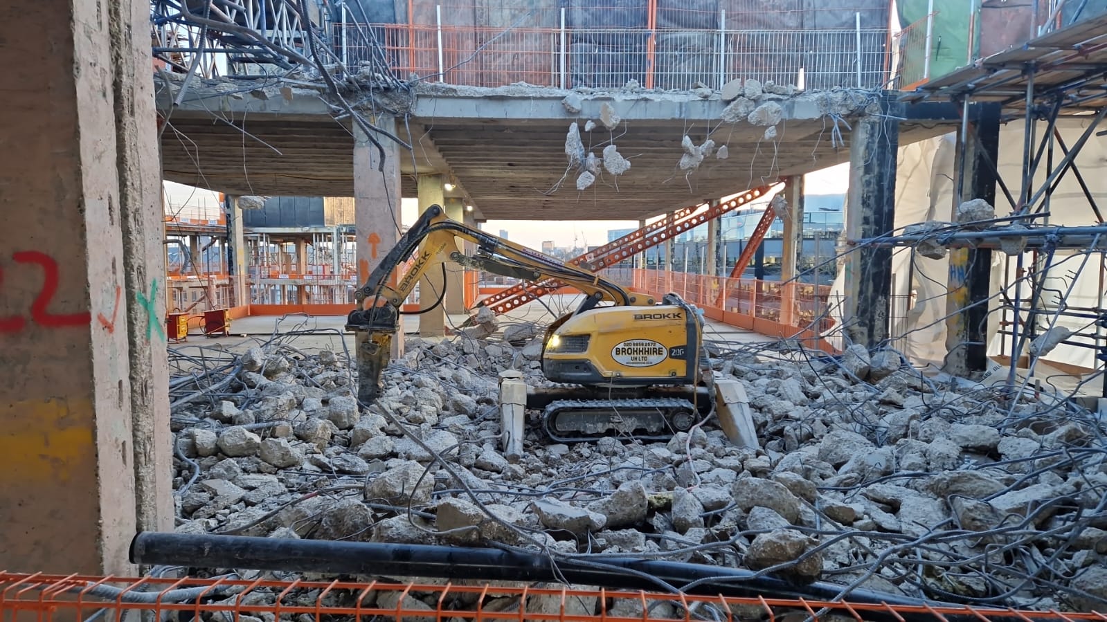Yellow demolition robot breaking concrete inside a partially demolished building, surrounded by rubble.