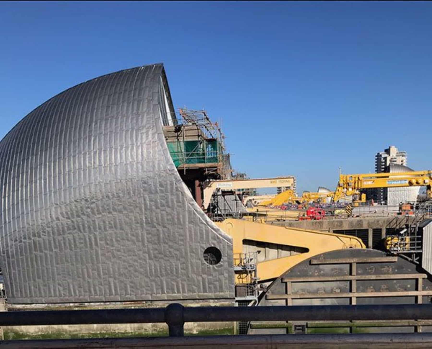 Large metal flood gate structure with cranes and construction equipment under a clear blue sky.
