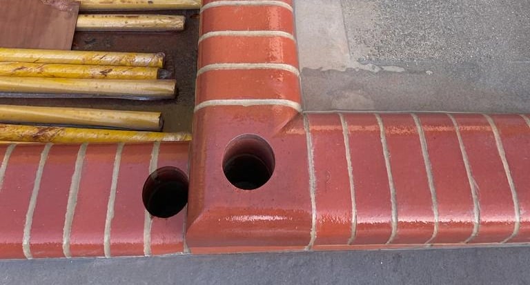 Red brick curb with two circular holes drilled at a corner; yellow rods lie nearby.