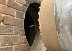 A large drill bit making a circular hole in a brick wall.