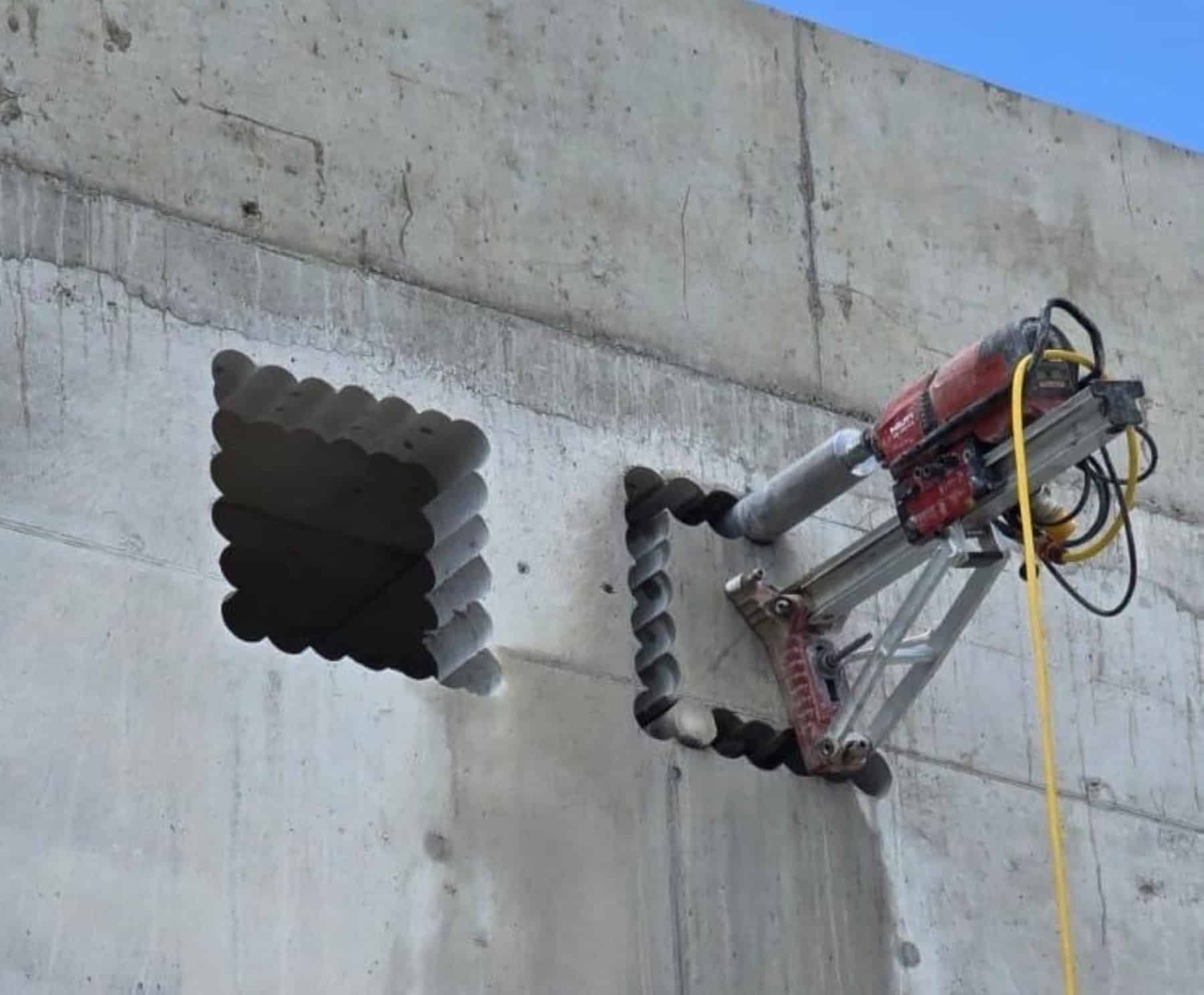 Drilling machine cutting a square hole in a concrete wall using diamond stitch drilling technique.