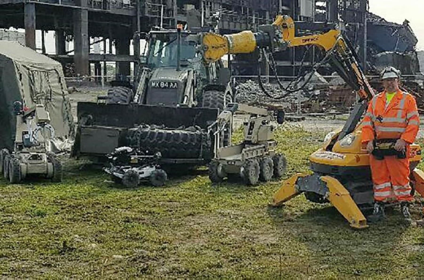 Person in high-visibility gear stands with demolition robots and machinery at an industrial site.