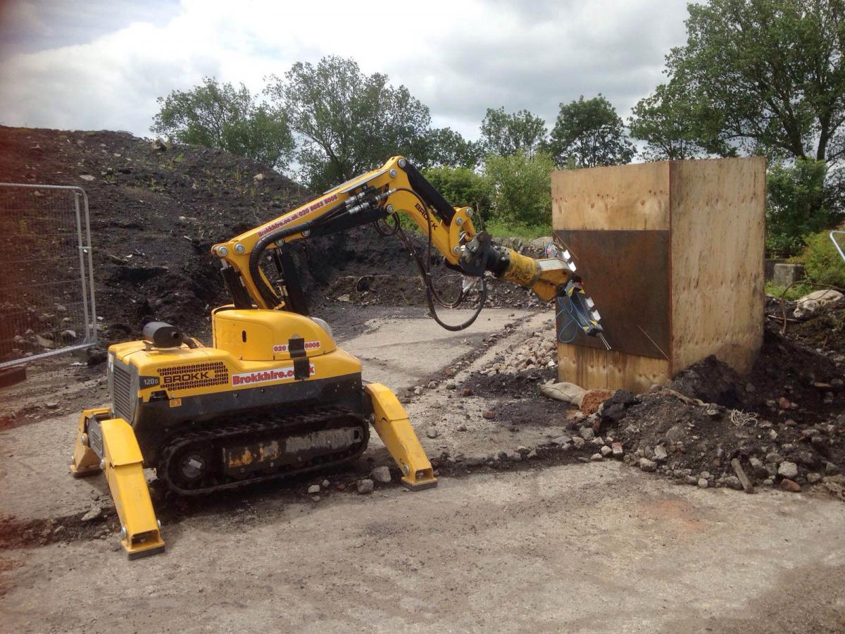 Yellow construction robot working near a wooden box at an outdoor excavation site.