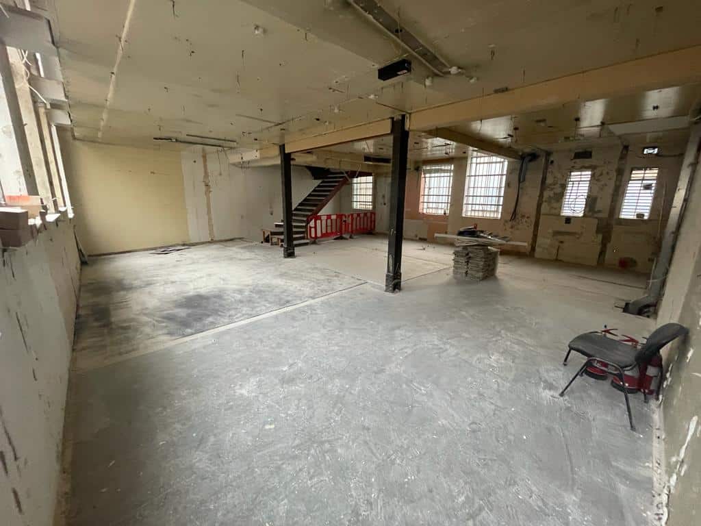 A large, empty, unfinished room with exposed beams, windows, and construction materials.