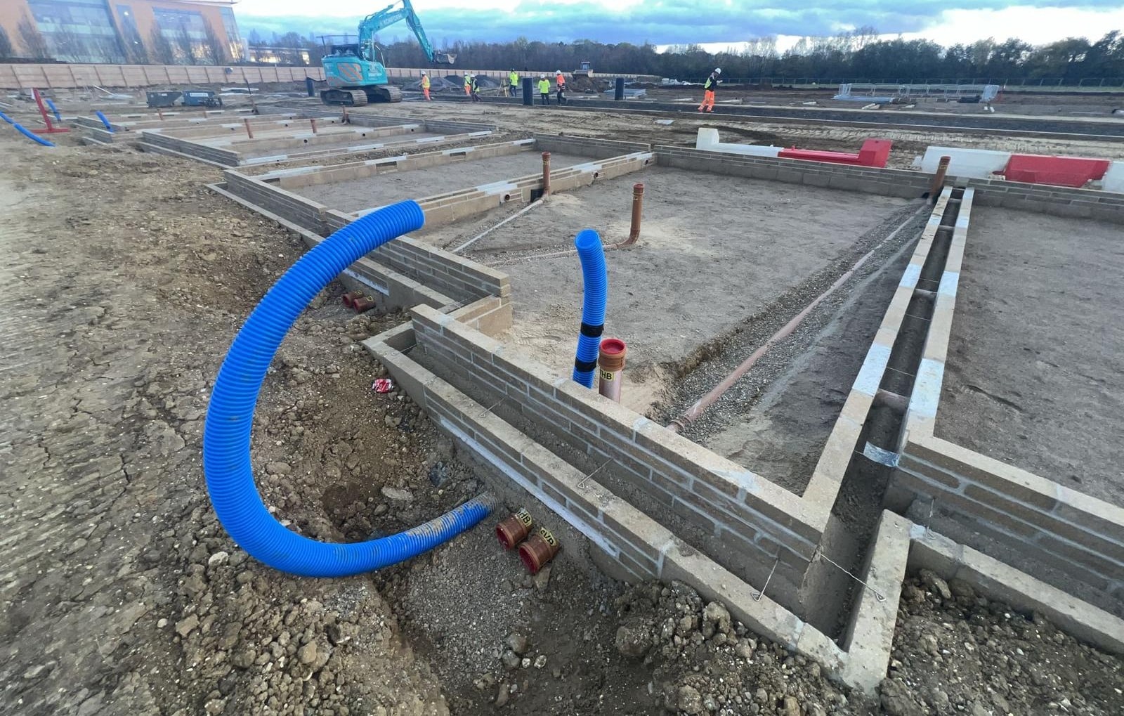 Concrete foundations with blue utility pipes at a construction site.