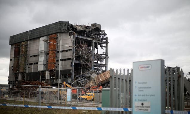 A partially collapsed industrial building behind a fence under a cloudy sky.