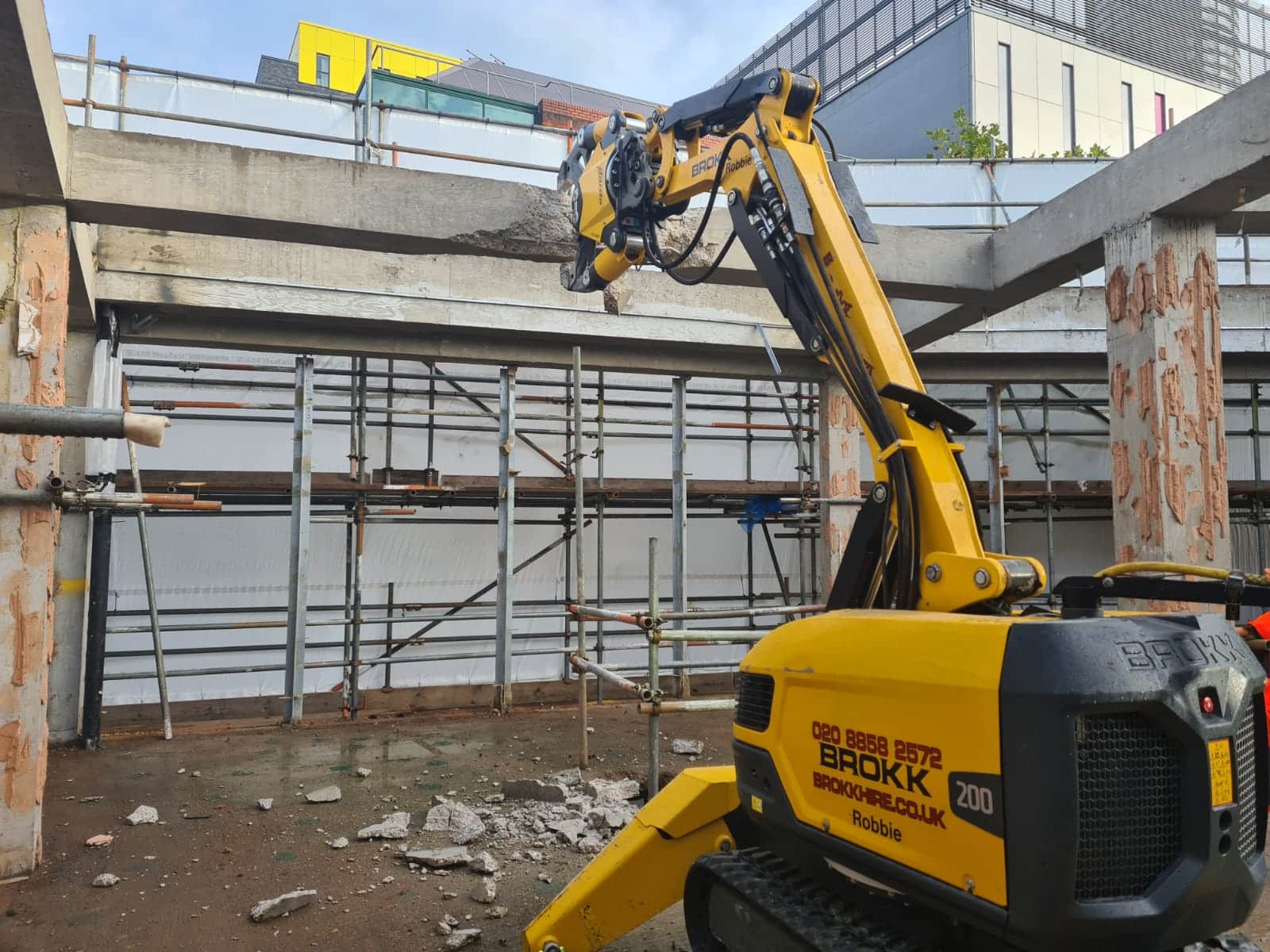 A yellow robotic machine crunches a concrete beam at a construction site.