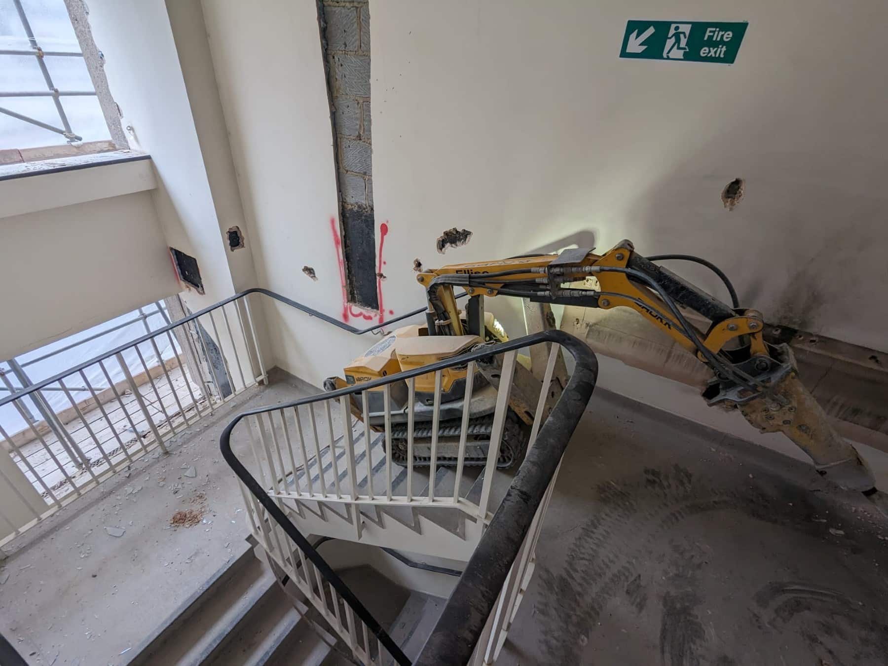A demolition robot breaks through a stairwell wall in a building under renovation.
