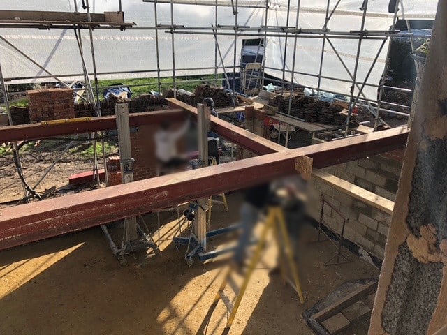 Steel beams being installed on a construction site with scaffolding and brickwork in progress.