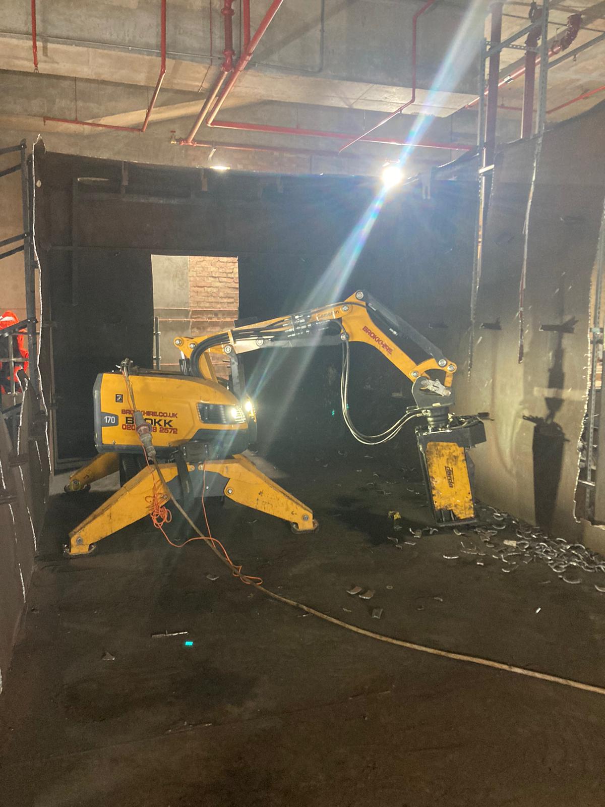 A yellow demolition robot breaking concrete inside a building under construction.