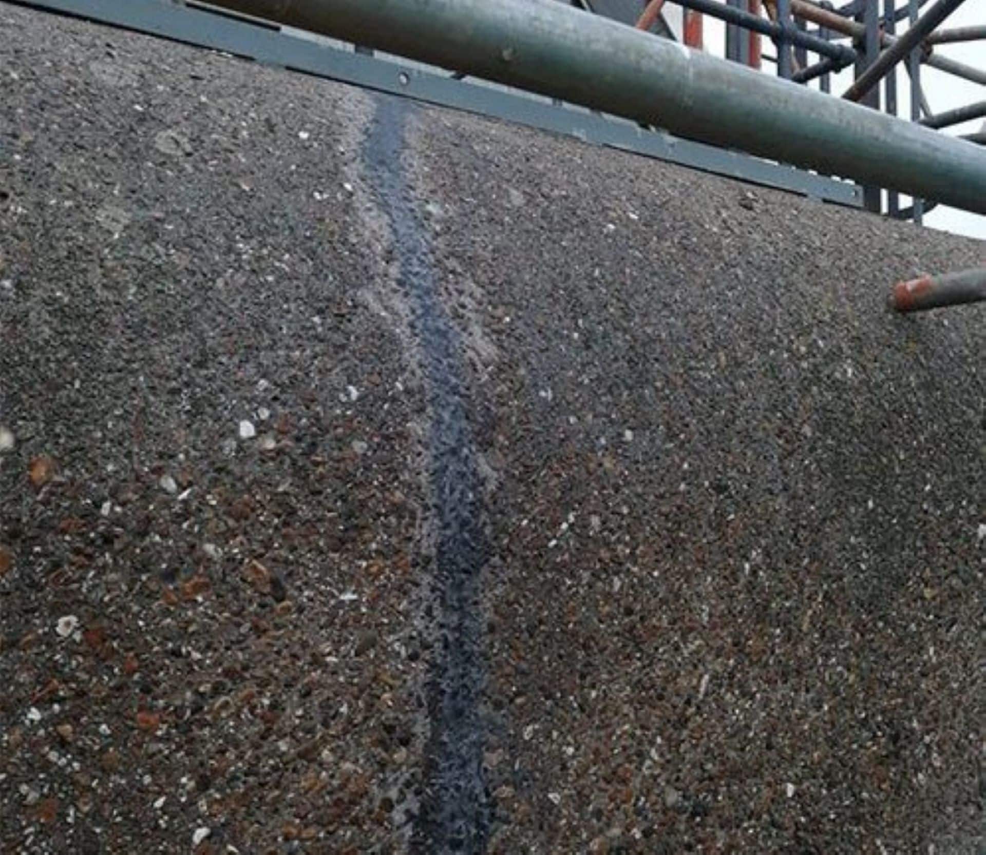 Crack in a concrete wall repaired with a visible sealant line, with scaffolding above.