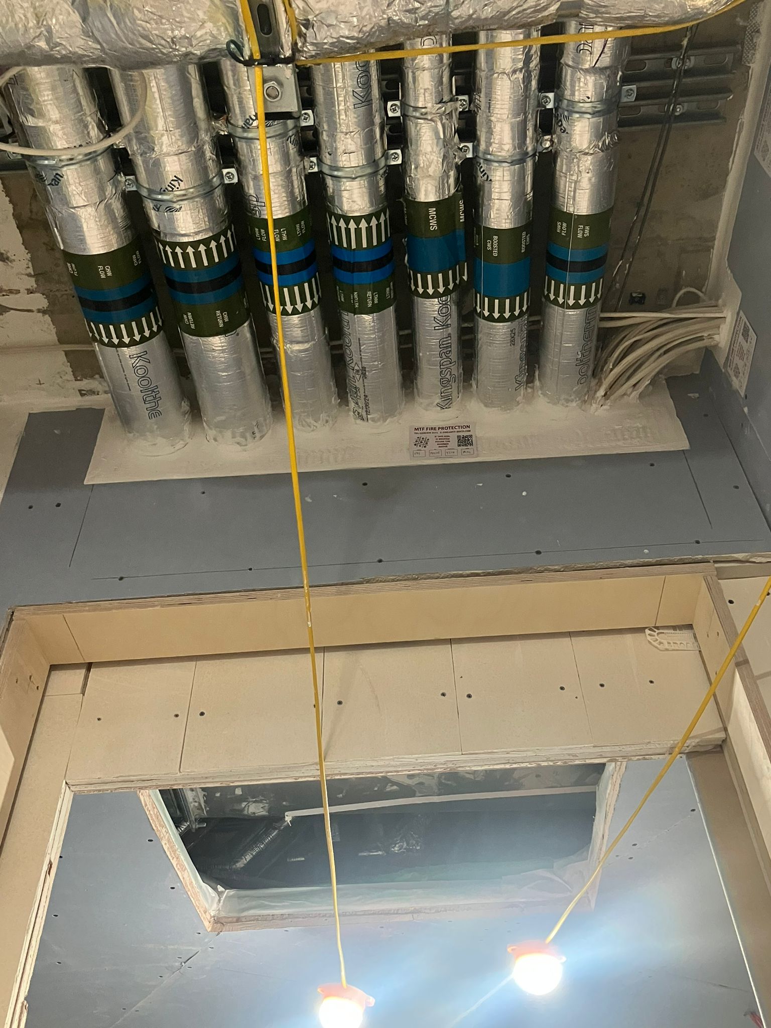 Five insulated metal pipes pass through a firestopped ceiling in a building under construction.