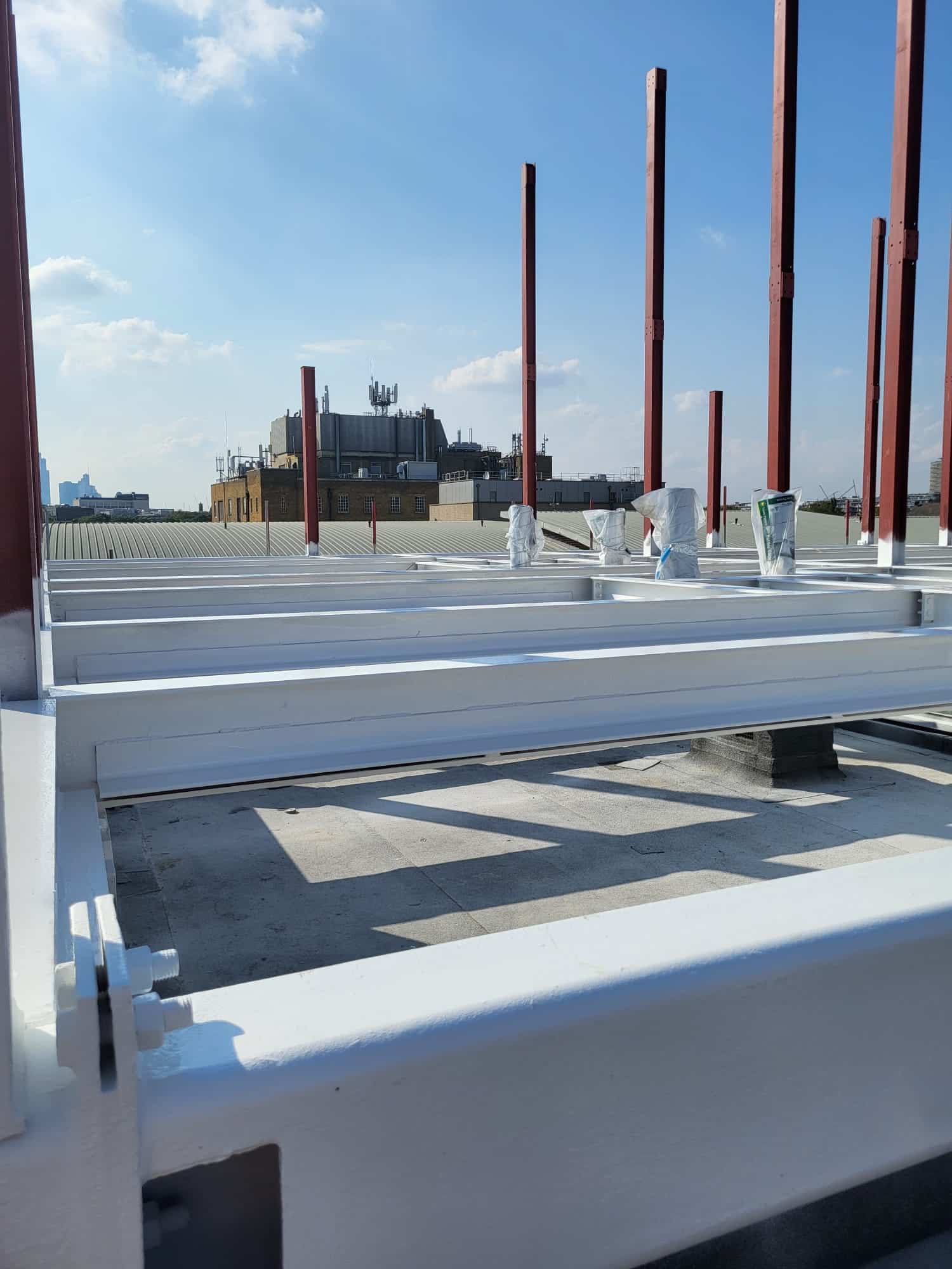 White metal beams and vertical red rods on a rooftop construction site under a blue sky.