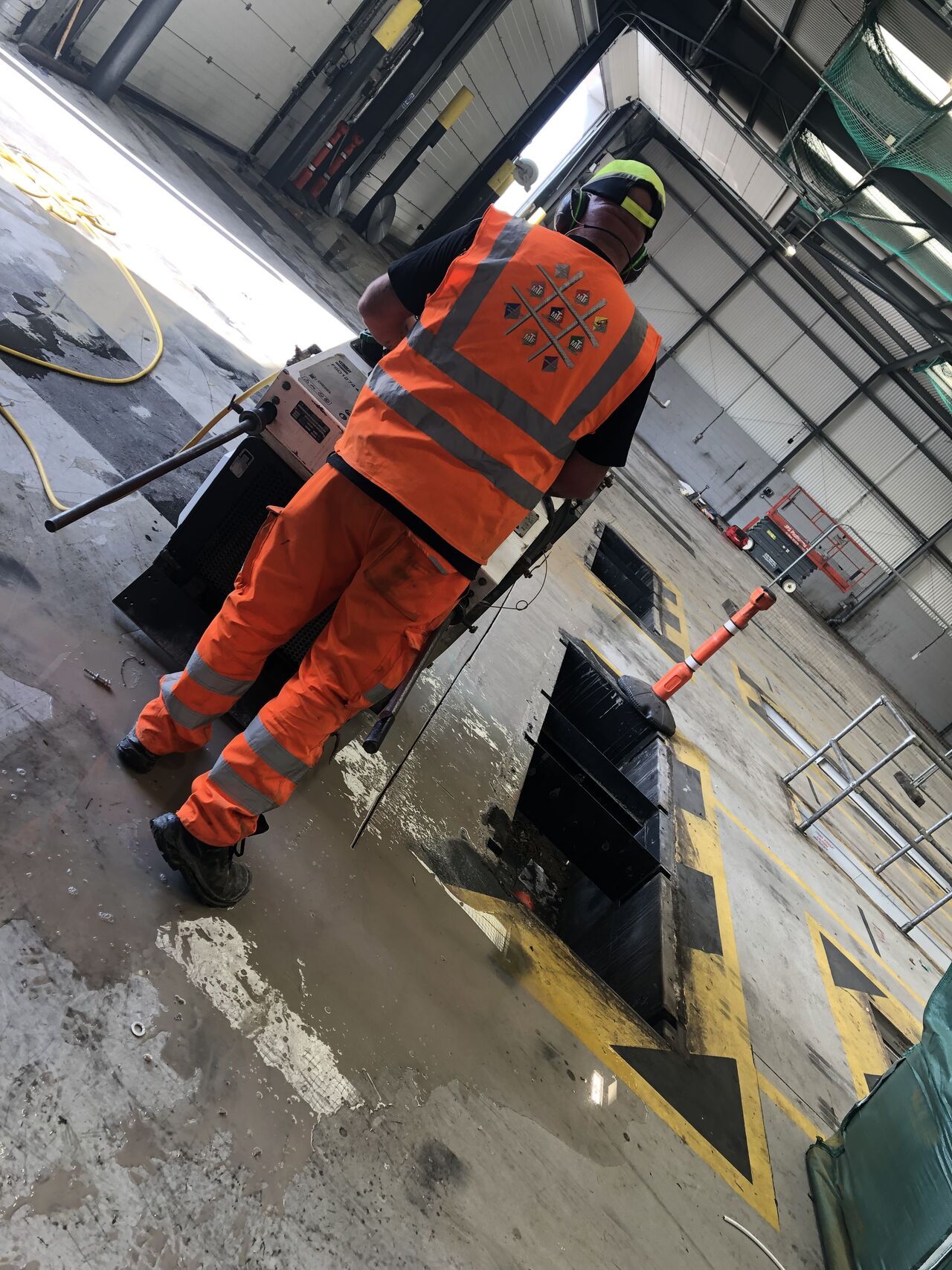 Worker in orange safety gear operating a floor saw in an industrial warehouse.