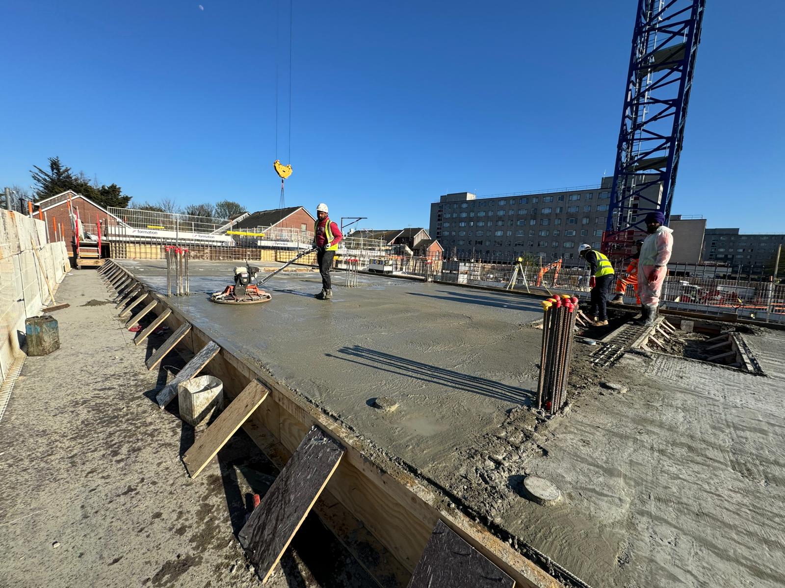 Workers smoothing wet concrete on a building foundation at a construction site.