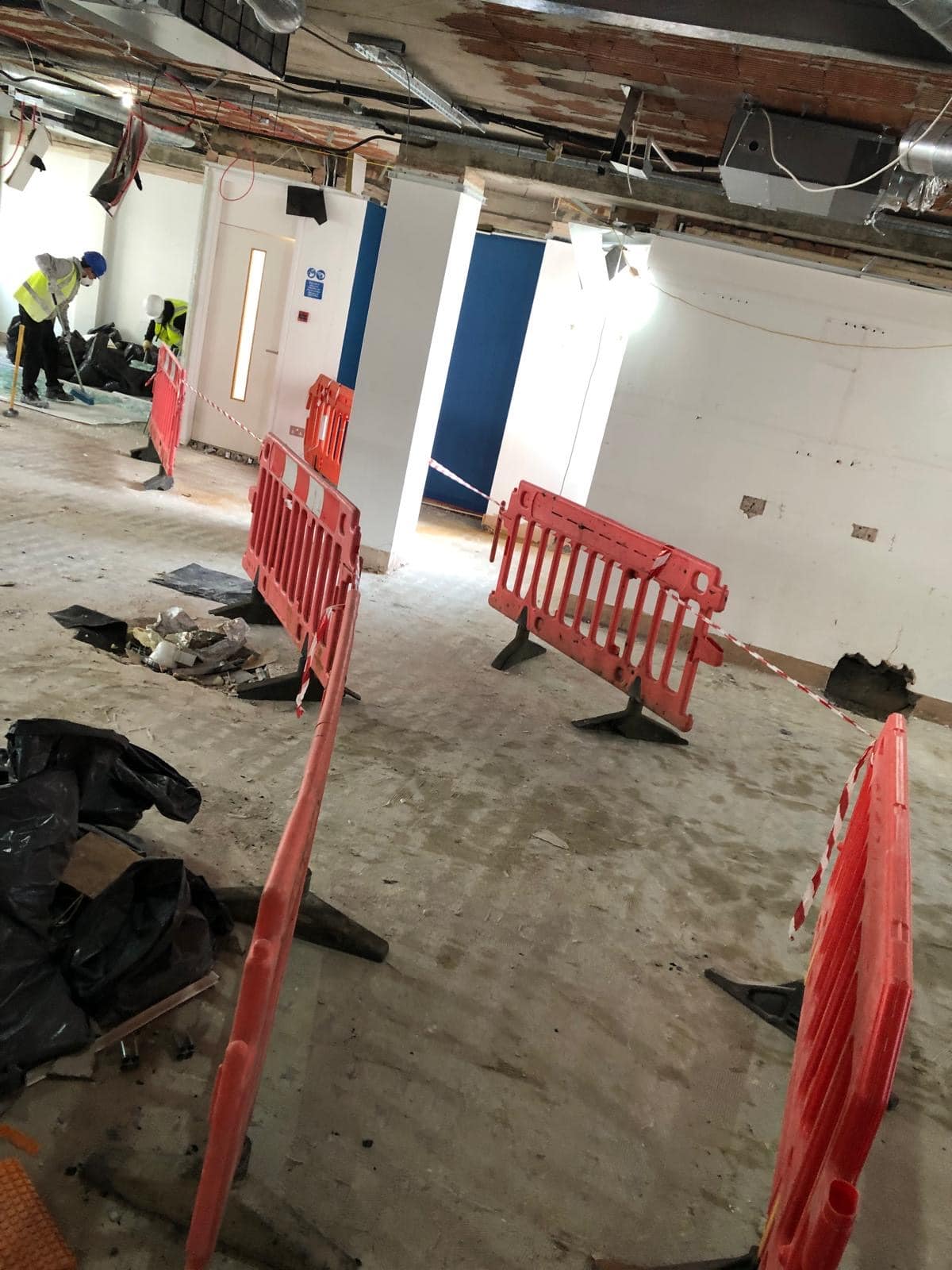 Construction site with orange safety barriers and workers in a partially finished room.