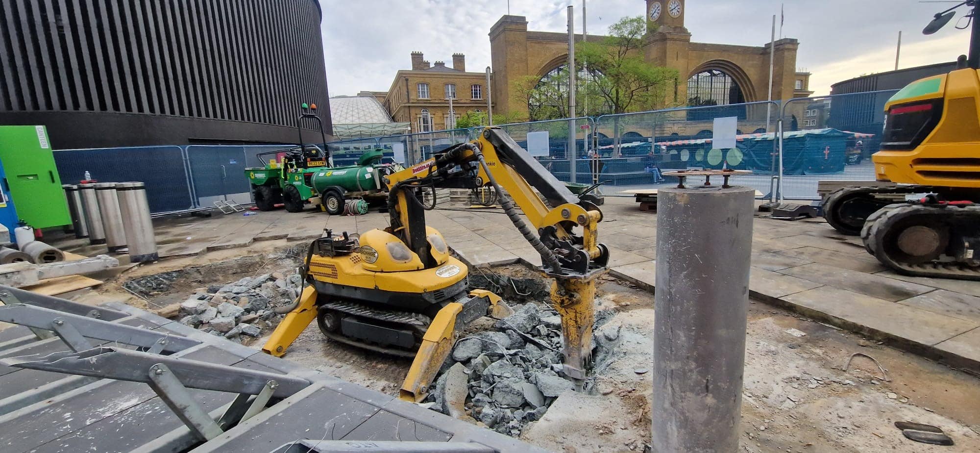 Yellow excavator breaking concrete at a construction site near King's Cross station.