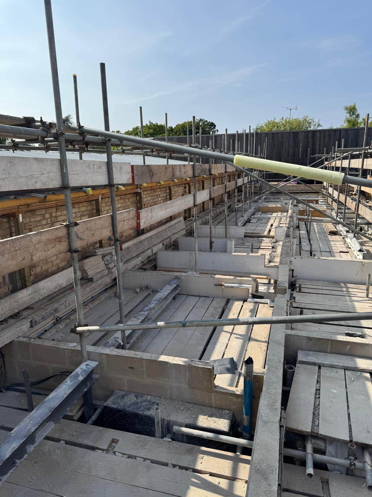 Construction site with exposed beams, scaffolding, and partial building framework under a clear sky.