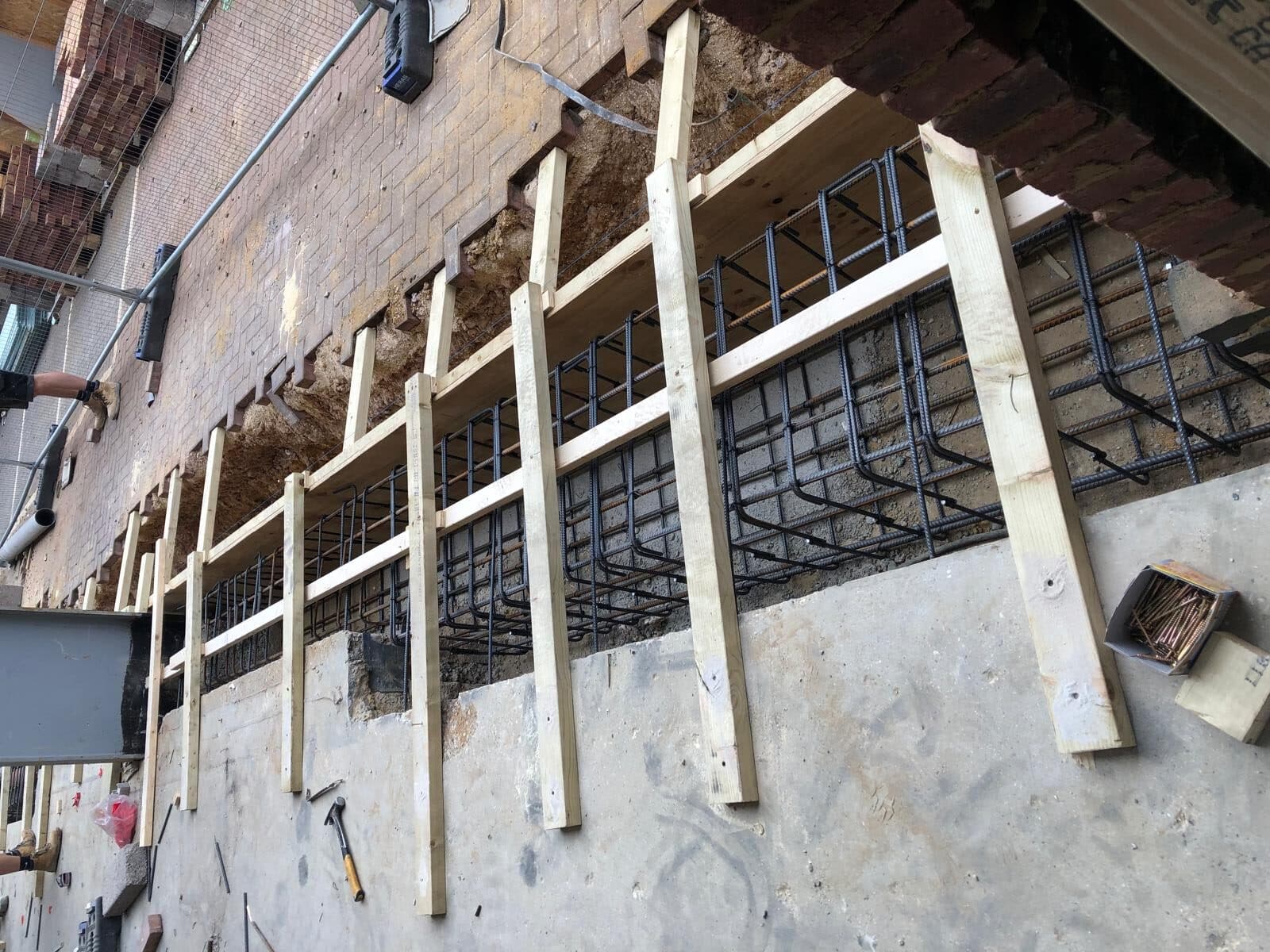 Wooden and steel framework for concrete construction against a brick wall.