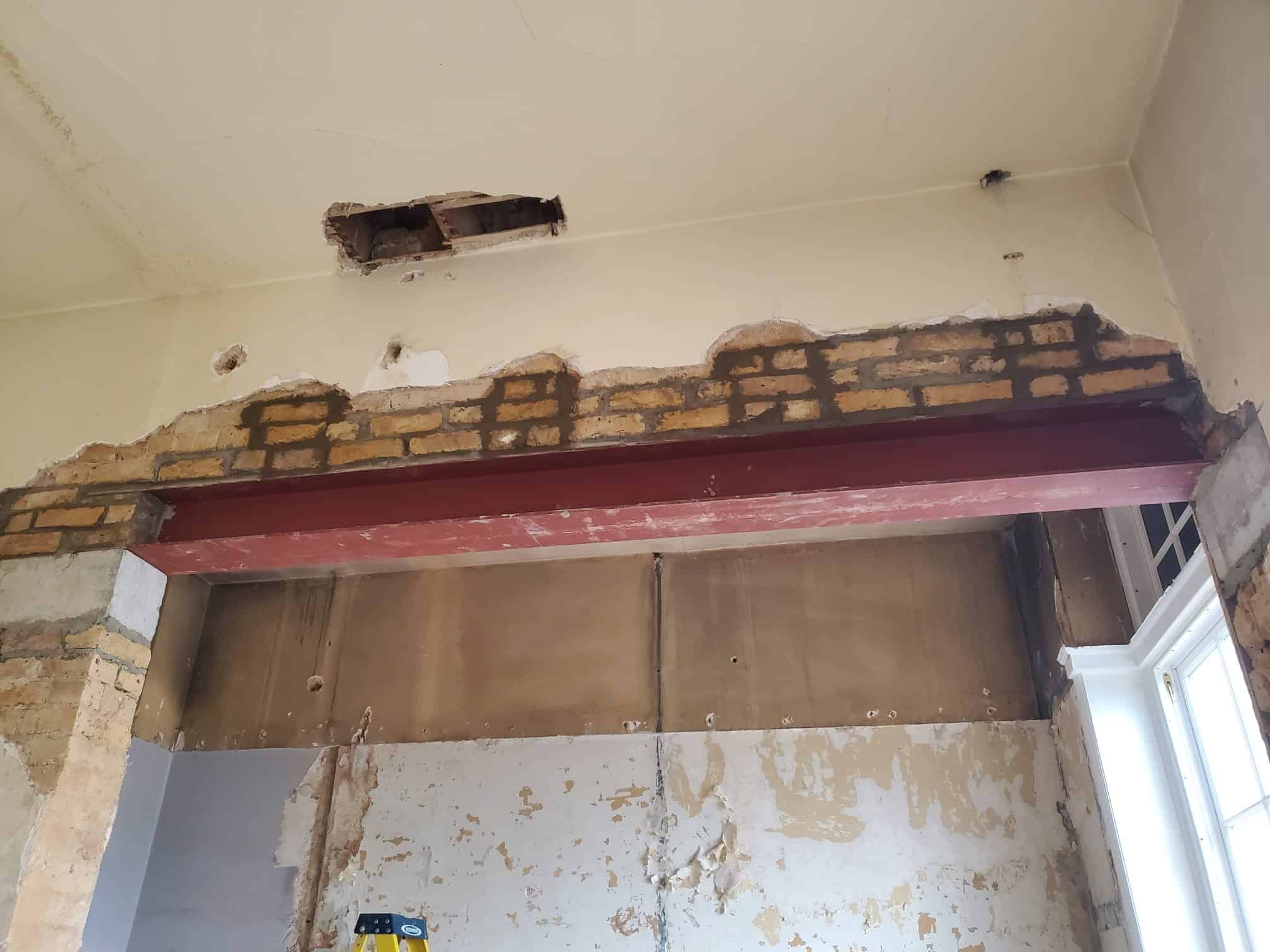 A steel beam is installed in a partially demolished brick wall inside a room.
