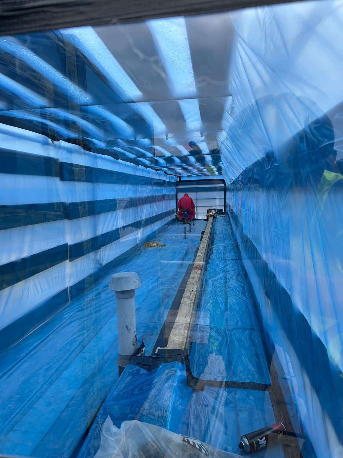 Worker in protective gear inside a blue plastic enclosure, possibly for asbestos removal.